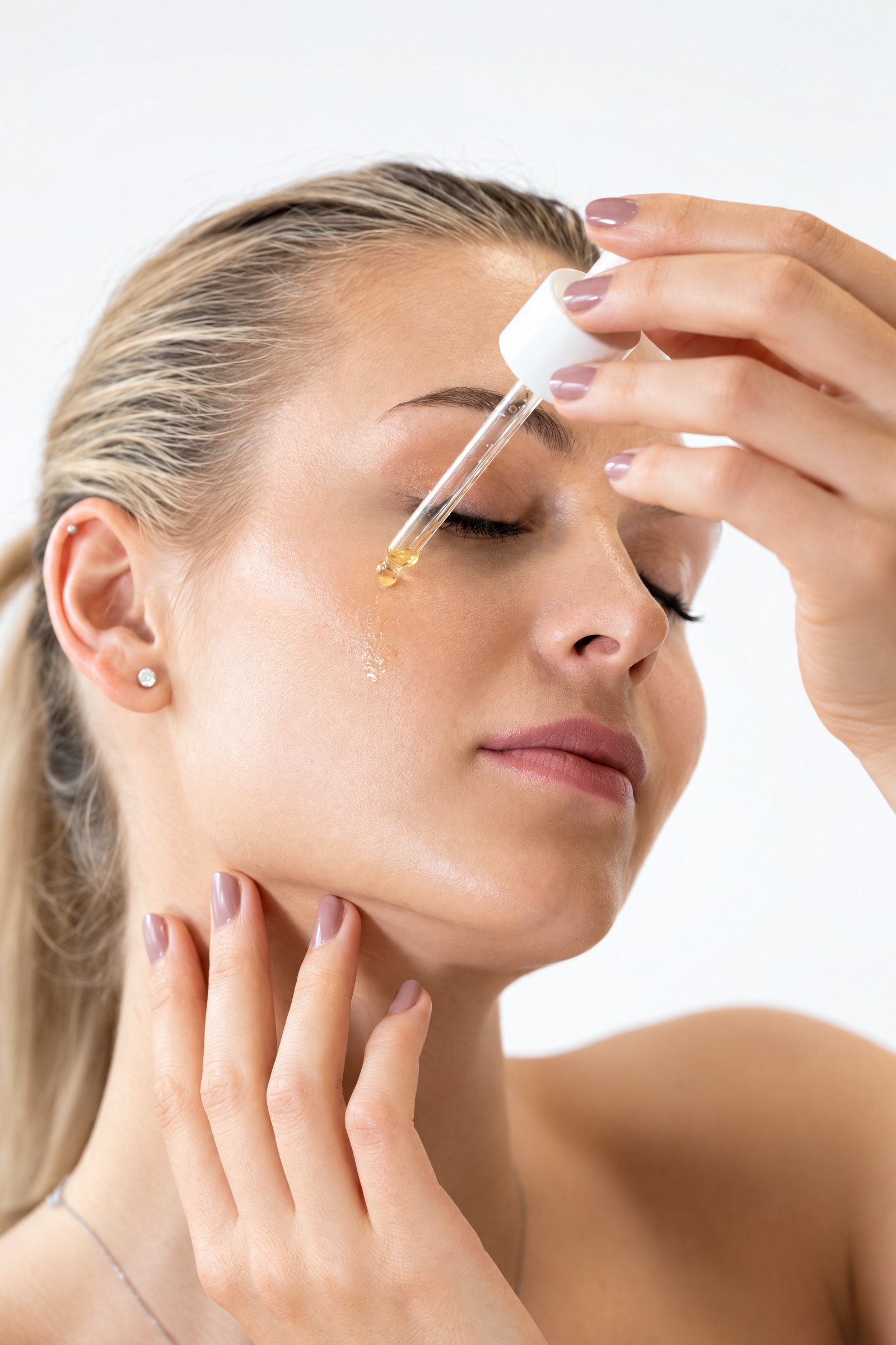 A woman applying a drop of hydrating serum to her face