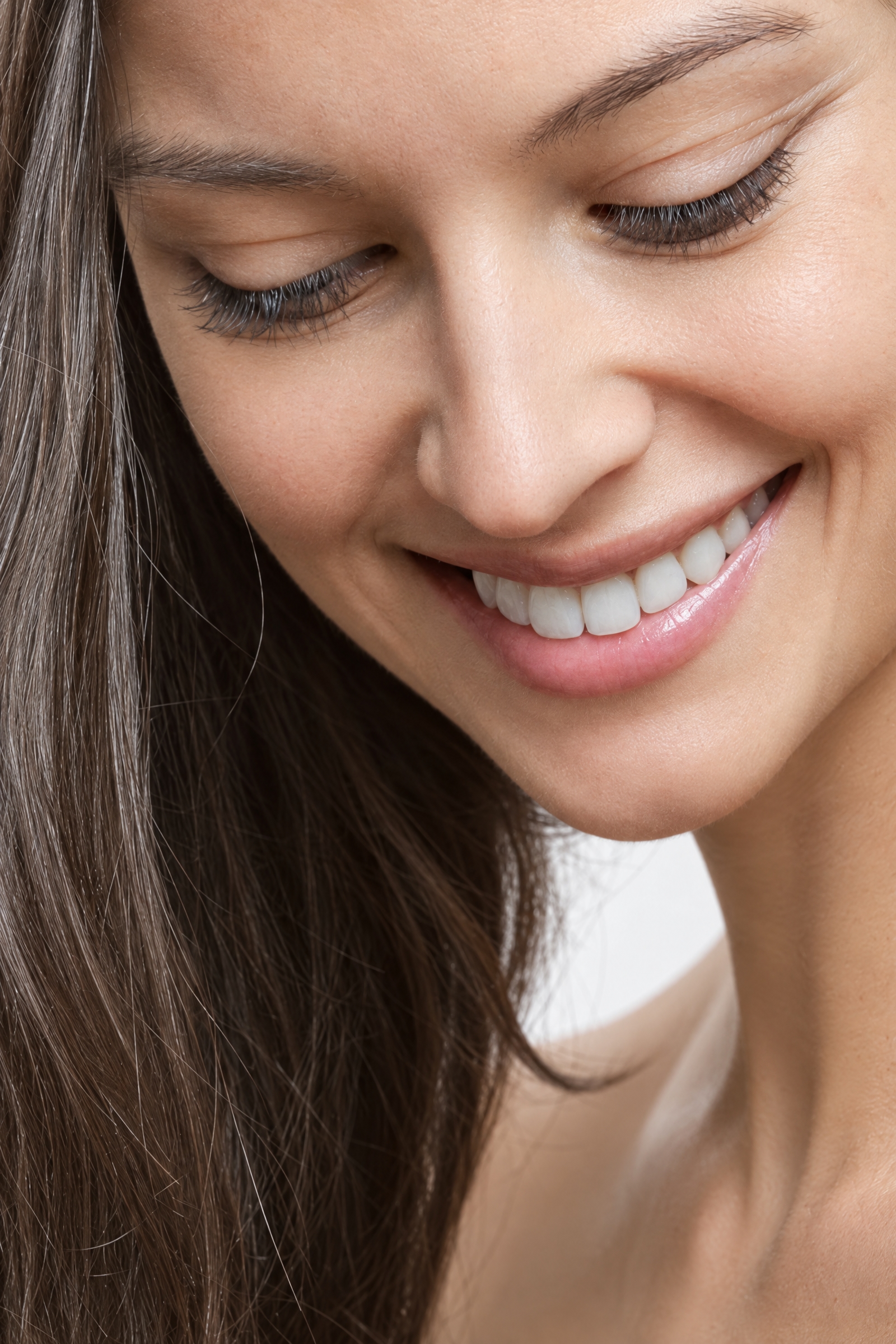 A woman smiling naturally, eyes lowered